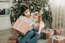 Beautiful mother and daughter in medical masks have fun at home near the Christmas tree in a white interior. Family happiness, holiday, joy, vacation, games with a woman. New Year's preparations. Cele
