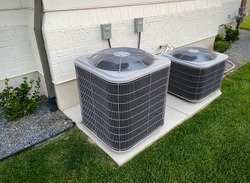 Double AC units outside white brick home with green landscape and gravel