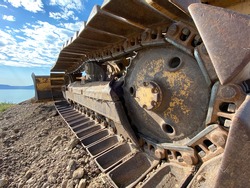 Closeup of treads on a bulldozer on a dirt road with blue sky