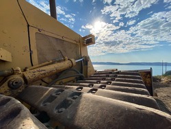 Closeup of old yellow bulldozer on dirt near lake with blue sky and lens flare