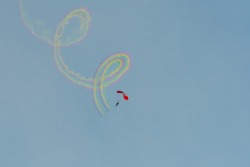 A parachutist  trailing rainbow smoke.