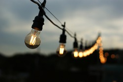 Glowing light bulbs hang in a row in the darkened sky.