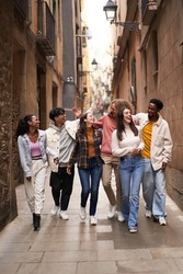 Vertical photo of a group of young happy friends walking in the street of the city. Smiling students laughing and having fun togethers