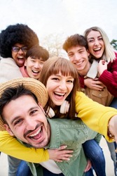 Vertical photo of Cheerful group of happy friends taking smiling selfie in piggyback. Three couple having fun together outdoors at park in the city. People enjoying travel in vacation holidays.