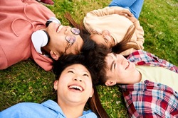 Close up shot of confident multiracial group of students smiling lying in a circle on the grass. Cheerful and happy young people having fun together. Diversity people spending leisure time.