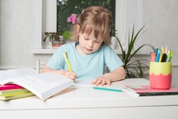 Girl sits at a table with books and a notebook and does her homework. Children learning at home. Back to school.