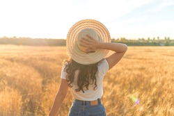 Young woman with a hat in a sunny ripe wheat field. Concept of prosperity and warmth.