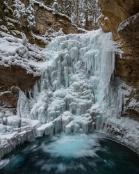 A partially frozen waterfall in a canyon with moving water at the base.