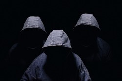 Three mysterious men silhouette with darkened face, no visible face, in blue hoodies on dark background
