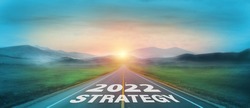 New year 2022 or start straight concept. Text 2022 and strategy written on the road with sunrise background. Concept of goal and challenge or career path, success, opportunity, change and hope.