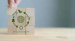 Circular economy concept, recycle, environment, reuse, manufacturing, waste, consumer, resource. 3rd.Sustainable development. Hand put wooden cubes; the symbols of circular economy on grey background.
