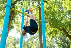 sports boy performs a coup on the horizontal bar in the park