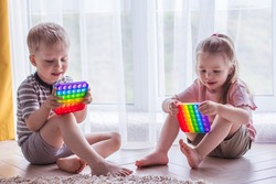 Blonde boy and girl Kids play with pop it sensory toy. Trendy silicon fidgeting game for stressed children and adults. Squishy soft bubble toys. Kid playing with rainbow color pop-it