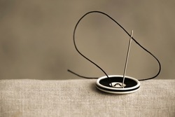 The black and white button is sewn with a sewing needle and black thread to hold the two fabrics together in close-up. A vintage-style photo for an article about the sewing hobby and sewing.