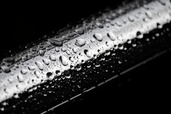 Dark background with metal chrome pipe covered with raindrops on black. Abstract background.