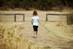 Back view of unrecognizable lonely girl walking away on stone ground in countryside