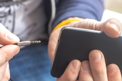  Close up view of Hand holding black mobile phone with earphone cable (plug, connection) stereo jack music port.