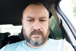 Portrait of an unshaven man 40 years old in a car. An ordinary man frowns at the camera.