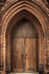 Detail of an ornate Victorian brick archway and wooden door of a church.