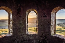 Ancient arch windows in a castle with scenic hills at sunset