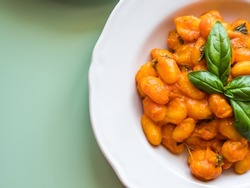 Italian potato gnocchi pasta with tomato sauce and melted mozzarella cheese, basil leaves. Cozy autumn winter lunch served in white dishes over green background