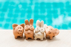 Happy animal clay family and friends, garden or house decoration, handmade rabbit and elephant with pig clay sculpture on swimming pool edge, outdoor day light
