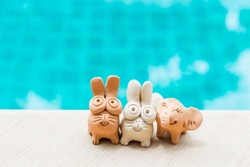 Happy animal clay friends on swimming pool edge, garden or house decoration, handmade rabbit and elephant clay sculpture, outdoor day light