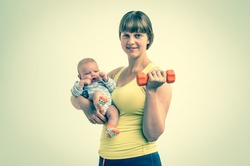 Happy young lady strengthens with dumbbell after childbirth and holds newborn baby - retro style