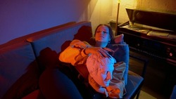 The girl is lying on the sofa and stroking the sculpture of the head. A model girl poses in front of the camera under the light of colored spotlights. Beautiful compositions with people in colored