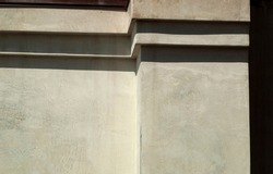Concrete gray-beige wall of the house with straight ledges of the type of steps in the upper part. Texture surface is visible. Minimalism and geometric. Bright sunlight, clear shadows. Horizontal.
