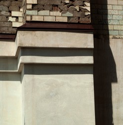 Part of the exterior wall of an old building with ledges like steps. Upper part is finished with tiles and concrete. Lower part is plastered. Different textures. Bright light. Neutral colors. Vertical