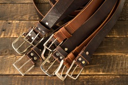 Lots of handmade men's leather belts on a wooden background. Classic men's leather belts in brown and cognac color. Handmade leather belts. Leather craft