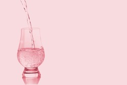 Pouring fresh water into wine glass with rose pink light effects background.