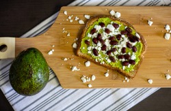 Overhead view of avocado toast with black beans and feta cheese on a wood cutting board