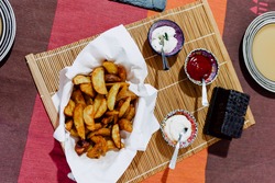 Paper towel basket filled with deluxe potato chips along with 3 containers of different sauces, ketchup, mayonnaise and yoghurt sauce. All on a wooden tablecloth. food photography.
