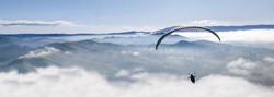 Paraglider flying high up in the air above the clouds and mountains on a sunny peaceful day