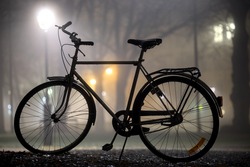 Silhouette of parked bicycle in park at foggy night in autumn