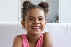 Closeup portrait of happy smiling african american girl child with cute hair buns looking at camera and laughing. Mixed-race daughter expressing positive emotion. Childhood and happiness concept