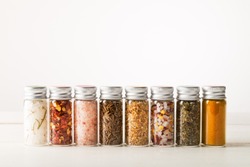 Spices Set in Mini Bottles, such as basil, turmeric, salts, chilli flakes, cumin seeds on light background 