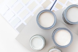 Tiny sample paint cans during house renovation, process of choosing paint for the walls, light grey and pastel colors, color charts and unit samples on background