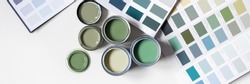 Tiny sample paint cans during house renovation, process of choosing paint for the walls, different green colors, color charts on background, banner size
