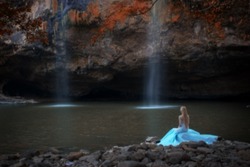 Gaussian blur image of young woman sitting near waterfall  