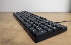 Black colored computer keyboard on an office table positioned on the perpendicular smoothly blurred in front and in the background. In detail the thread coming out to the right corner.