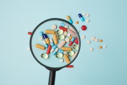 Creative medical layout made with pharmaceutical medicine pills, tablets, capsules under the magnifying glass on pastel blue background. Minimal modern pharmacy or health care concept. Flat lay.