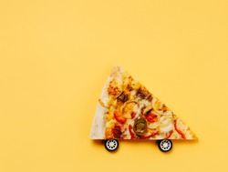 Pizza slice moves with wheels against pastel orange background. Creative food delivery concept. Restaurant or pizzeria banner. Flat lay, top view.
