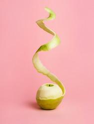 Half peeled fresh green apple with flying peel on pastel pink background. Creative fruit concept with copy space. Surreal food composition.