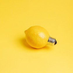 A single fresh lemon as a light bulb isolated on a bright yellow background. Trendy fruit idea. Abstract and surreal healthy diet. Creative food concept.