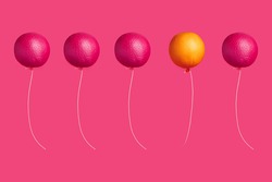Magenta pink fruit balloons and one orange balloon flying in the air on a pink background. Individuality, think different and leadership composition. Creative food idea.