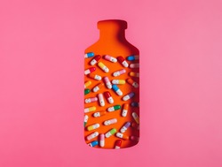 Orange bottle container as a remedy for illnesses with colorful pills isolated on a pink background. Medicine and drug inspired photography. Doctor's prescription. Creative pharmacy concept. Flat lay.
