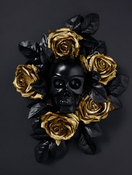 Black skull surrounded with golden rose flowers and black leaves isolated on a black background. Creative Halloween or Santa Muerte concept. Minimal dark romantic idea. Flat lay.